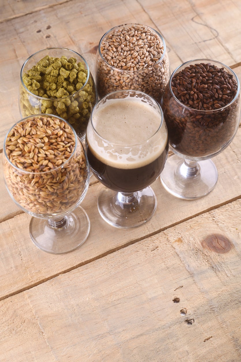 Glasses filled with dark beer, different malts and hops over a wooden background
