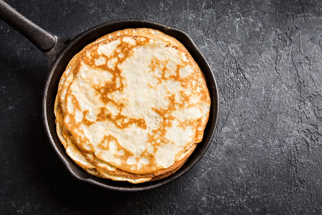 Homemade crepes in cast iron pan over rustic black background with copy space - cooking fresh homemade breakfast crepes pancakes food