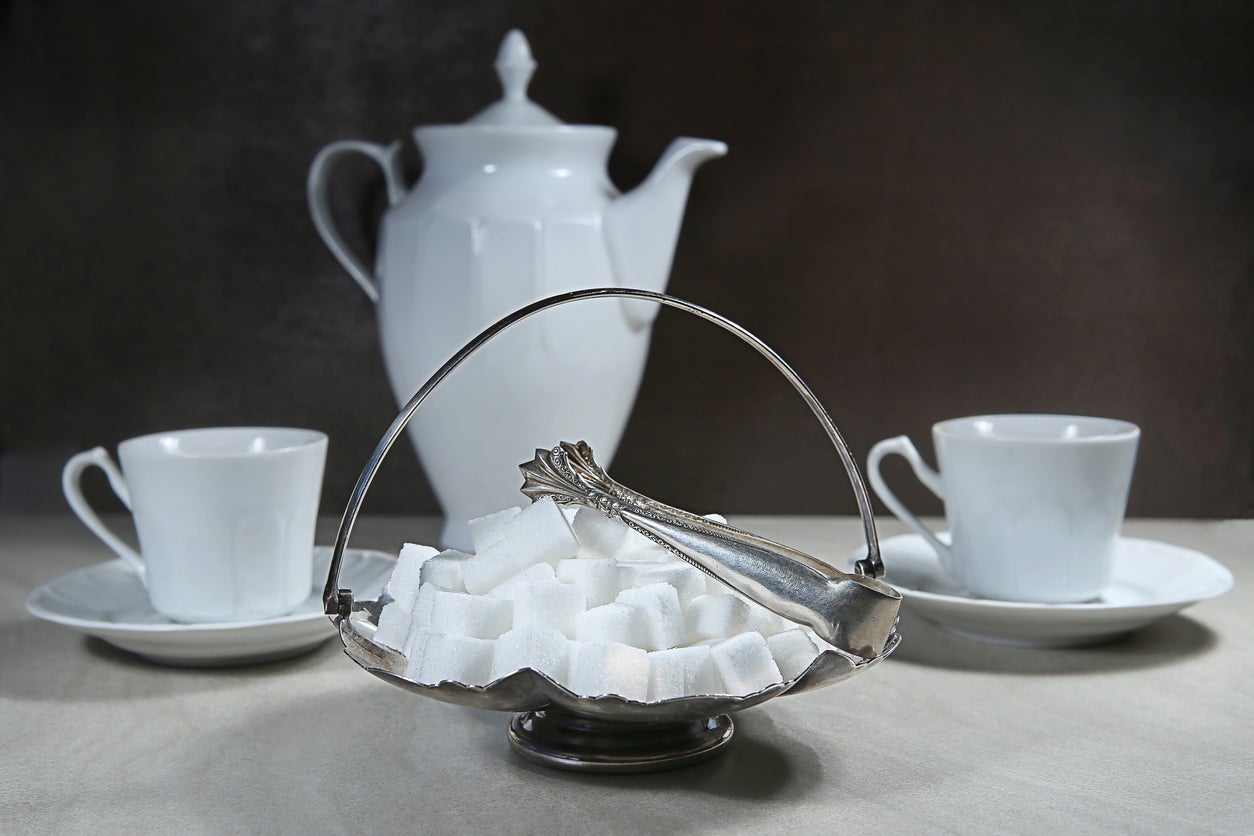 Retro sugar bowl with sugar tongs and cups with coffee or tea pot.