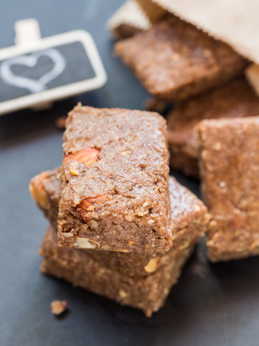 Homemade organic healthy chewy muesli granola power bars with wholemeal oats, cashew butter, honey and nuts, cut into bite size, falling out of a paper bag, arranged in a small pile on a dark background. Vertical orientation, close up, plate with drawn heart shape in the background.