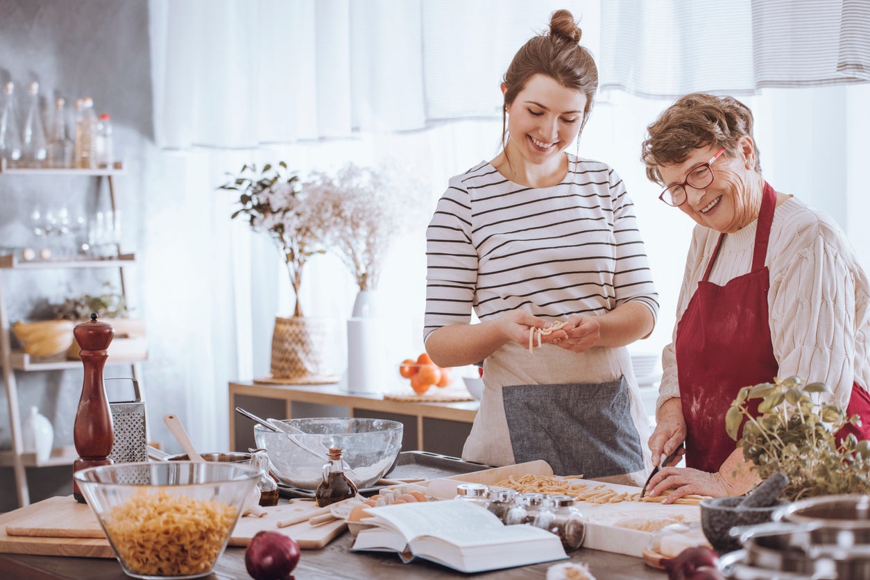 Smiling young woman shaping dough and happy grandmother cutting it