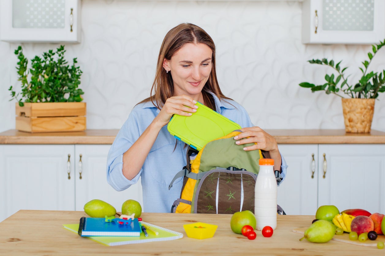 Healthy food concept. Mother packing lunch box into a kid's backpack in the kitchen.