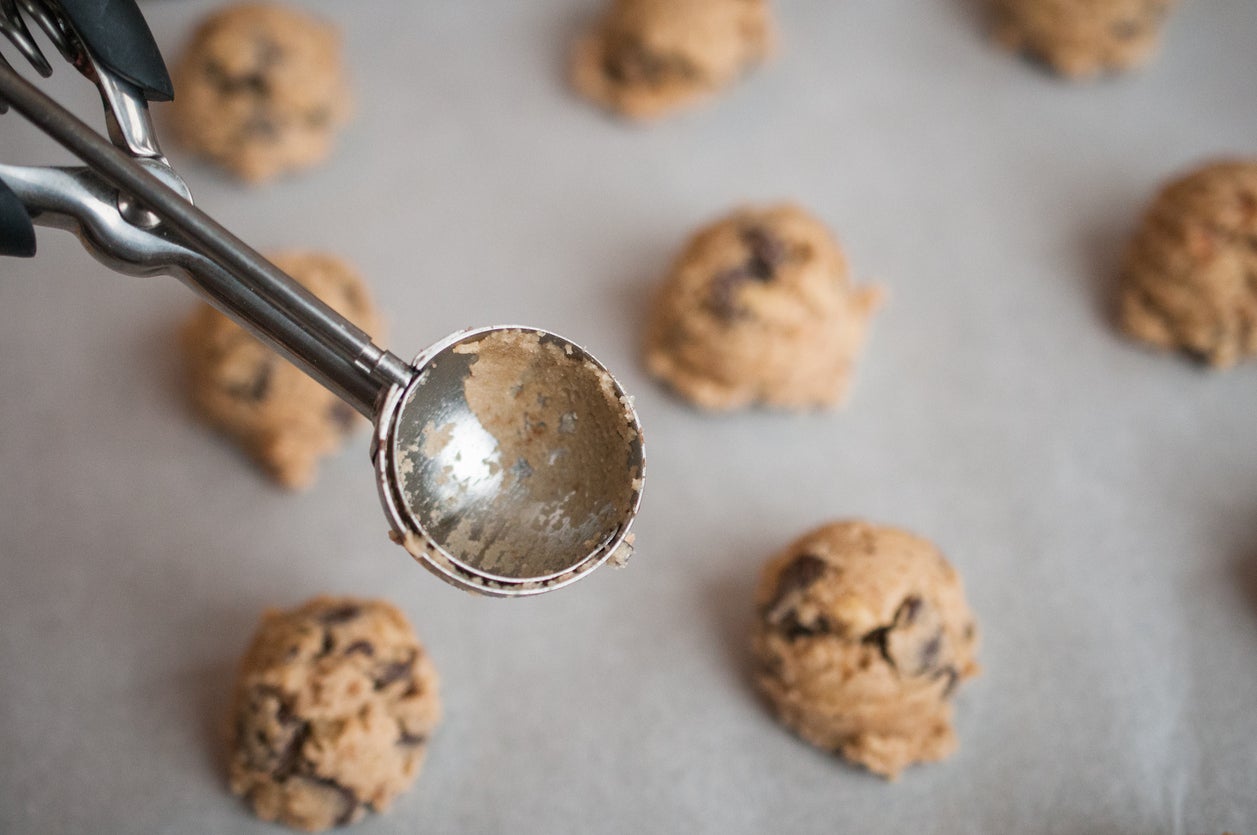An overhead photograph of a baking pan with raw chocolate chip  cookies dough 
and scoop