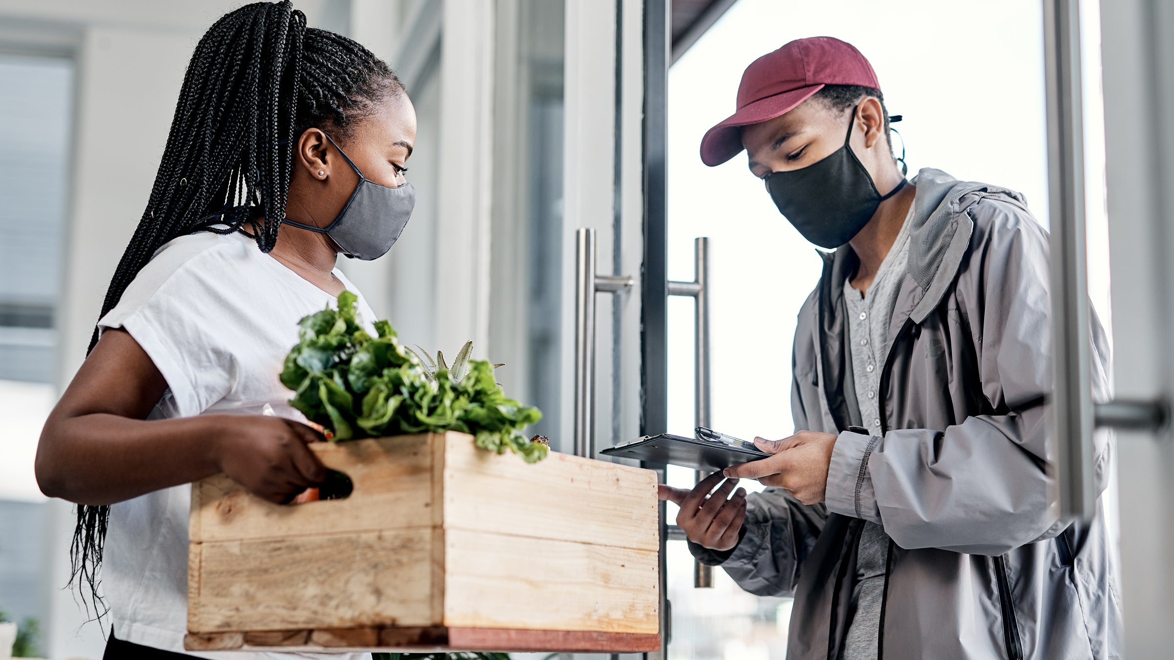 Masked woman holding a crate of vegetables with a masked man looking at a clipboard